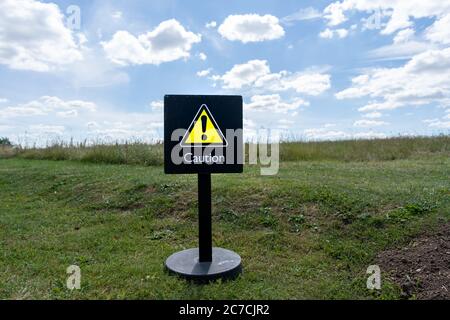 Un segno di attenzione giallo in un campo verde sotto un cielo blu. Ecologia, avvertenza ambientale. Foto Stock