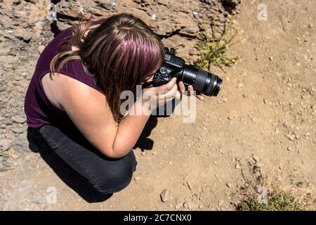 Bambino caucasico leggermente abbronzato con acconciature di capelli viola a strisce sul terreno fotografando un soggetto basso Foto Stock