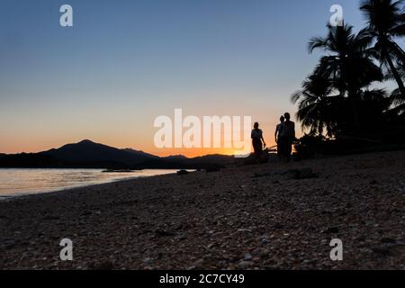 Gente che balla e gioca su una spiaggia in Madagascar, alberi fiancheggiati e barche galleggianti in mare al tramonto, Madagascar Foto Stock