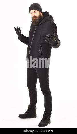 Ragazzo elegante in giacca e cappello, isolato su sfondo bianco. L'uomo con barba indossa un abito invernale nero e brutale. Concetto di outfit invernale. L'hipster con il viso premuroso indossa abiti caldi. Foto Stock