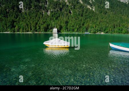 Piccola barca sul lago cristallino Plansee nelle Alpi europee, in Austria all'alba della mattina presto Foto Stock