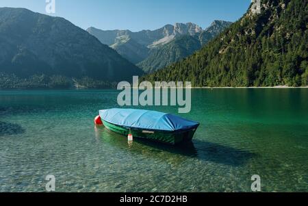 Piccola barca sul lago cristallino Plansee nelle Alpi europee, in Austria all'alba della mattina presto Foto Stock