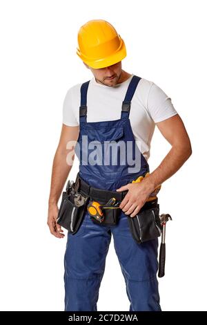 Giovane uomo di riparazione caucasico in casco giallo e uniforme. Uomo di mano indossando cintura utensile isolato su sfondo bianco studio Foto Stock