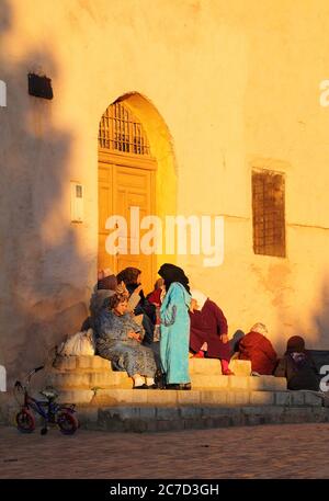 Un gruppo di donne marocchine, tipicamente vestite, seduti su gradini nel tardo pomeriggio del sole invernale. 22 dicembre 2013 a Meknes, Marocco. Sito UNESCO. Foto Stock