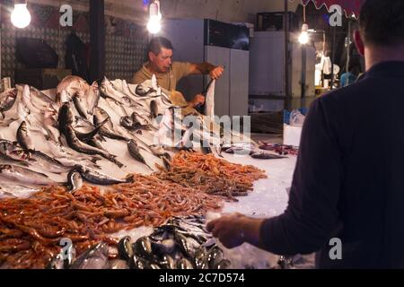 CATANIA, ITALY - Oct 15, 2016: Pescatore che pulisce il pesce per un cliente in attesa, che sta cercando. Mercato, Catania, Sicilia, Italia Foto Stock