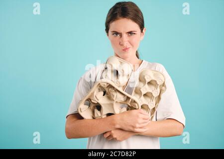 Ragazza confusa che tiene cartoni spazzatura in mani pensieroso guardando in macchina fotografica su sfondo colorato isolato Foto Stock