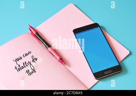 Smartphone e notebook rosa su tavolo blu. Foto Stock