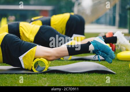 Laminazione della schiuma. Gruppo di giovani giocatori di calcio in scarpe da calcio usando il rullo in schiuma da training sulla sessione di allenamento. Stretching e riscaldamento dei muscoli Foto Stock