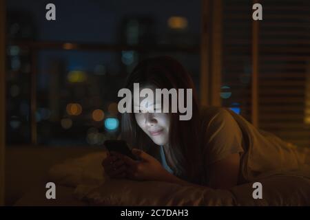 Donna asiatica che dorme e utilizza smartphone per social network o videoconferenza quando Covid19 focolaio, quarantena e panne di Coronavirus Foto Stock