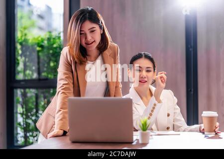 Due donne d'affari asiatiche che lavorano con il business partner tramite computer portatile tecnologico in una moderna sala riunioni, ufficio o spazio di lavoro, pausa caffè, partner Foto Stock