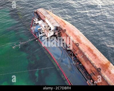 Una petroliera arrugginita si è arenata. Disastro ambientale e fuoriuscita di petrolio in mare vicino al mare. Vecchia nave sullo sfondo del mare smeraldo. Foto Stock