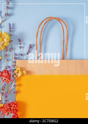 Un sacchetto di carta giallo con spazio per scrivere e asciugare fiori su sfondo blu Foto Stock