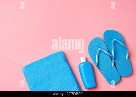 Asciugamano blu, bottiglia cosmetica con crema solare e infradito su sfondo rosa Foto Stock
