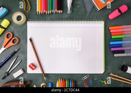 Apri il notebook con un foglio di linee e materiale scolastico intorno su una lavagna verde Foto Stock