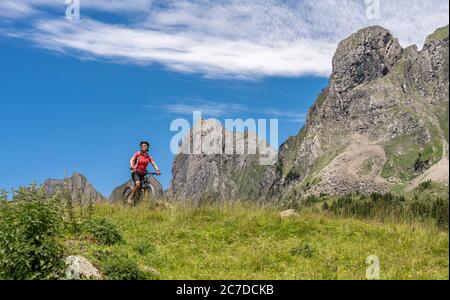 Donna anziana attiva in sella alla sua mountain bike elettrica sotto le sette cime di Churfirsten nel Cantone di San Gallo, Svizzera, paesaggio Foto Stock