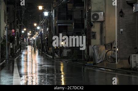 Vista notturna di una strada vuota immersa nella pioggia illuminata da lampioni in una parte suburbana della Tokyo occidentale Foto Stock