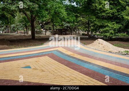 Posa di lastre di calcestruzzo colorate nel parco. I lavoratori professionisti che lavorano su muratori stanno installando nuove piastrelle e lastre per pavimentazione per marciapiede su piani Foto Stock