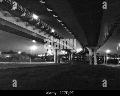 Immagine in scala di grigi a basso angolo di un'autostrada con colonne circondate da luci di strada di notte Foto Stock