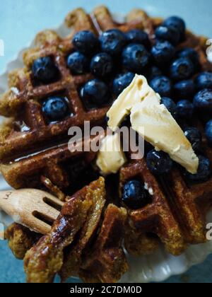 Primo piano verticale di un waffle dolce con sciroppo, mirtilli e burro. Foto Stock