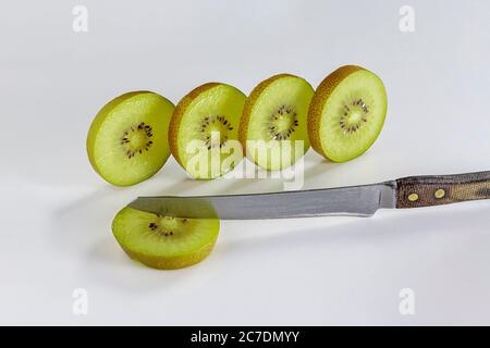 Quattro sottili fette di kiwi affettate si trovano su uno sfondo bianco e un coltello si trova vicino Foto Stock