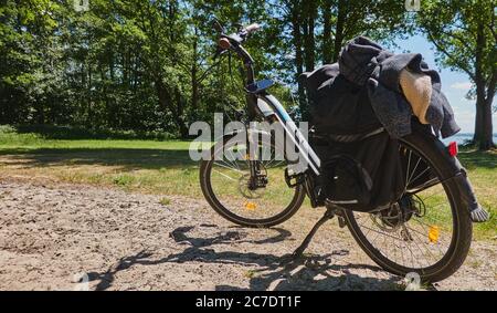 Steinhude, Germania, 29 maggio 2020: Bicicletta elettrica con carico e uno smartphone collegato per la navigazione è parcheggiata su una strada sterrata accanto a un prato. Foto Stock