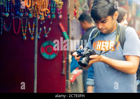 Giovane fotografo indiano che scatta guardando la sua macchina fotografica nel mezzo del mercato nella città collinare di mcleodganj in India himachal pradesh Foto Stock