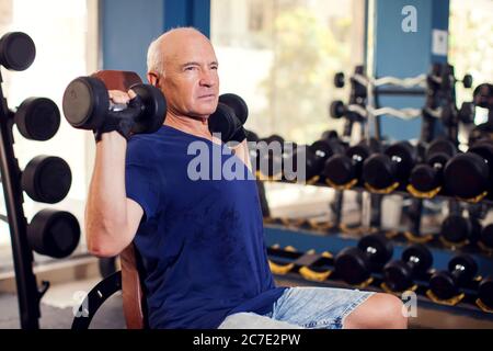 Un ritratto di calvo uomo anziano in palestra allenando con manubri. Concetto di persone, salute e stile di vita Foto Stock