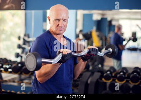 Un ritratto di calvo anziano in palestra allenando con barbell. Concetto di persone, salute e stile di vita Foto Stock