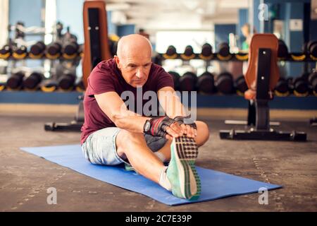 Un ritratto di calvo uomo anziano che fa stretching dopo l'allenamento in palestra. Concetto di persone, assistenza sanitaria e stile di vita Foto Stock
