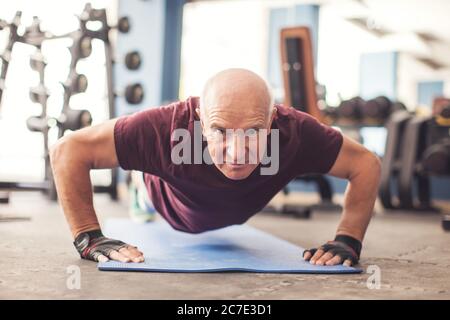 Un ritratto di calvo uomo anziano che fa gli spintups esercitarsi nella palestra. Concetto di persone, assistenza sanitaria e stile di vita Foto Stock