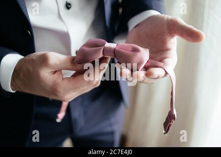 Cravatta rosa nelle mani dell'uomo. Primo piano. Accessori per uomo da sposa Foto Stock