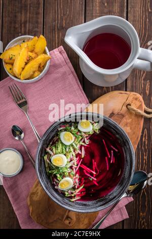 Zuppa di barbabietole fredde con uova, patate al forno, souce, rustico sfondo in legno, caraffa bianca, tovaglia rosa, vista dall'alto Foto Stock