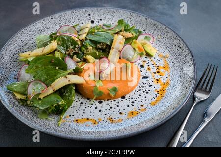 Insalata con verdure verdi e mini-mais alla griglia con ricotta e mousse di pomodoro. Piatto vintage, cucchiaio e forchetta su sfondo grigio. Foto orizzontale. Foto Stock