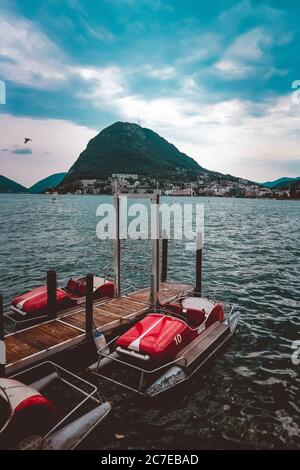 Pedalò vicino ad un molo di legno sul mare circondato da belle montagne verdi sotto il cielo nuvoloso Foto Stock