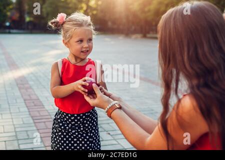 Giovane madre che dà alla figlia mela all'aperto scuola primaria. Piccolo allievo pronto per le lezioni Foto Stock