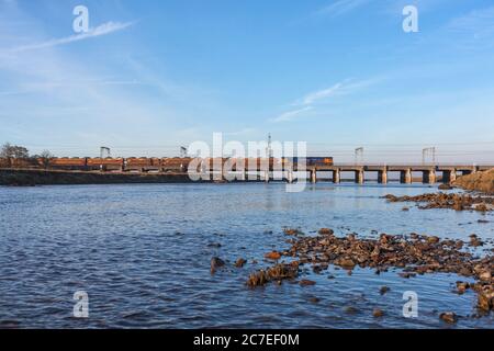 GB Railroad classe 66 locomotiva che attraversa il viadotto del ponte metallico a Mossband sulla linea principale della costa occidentale con un treno merci che trasporta auto nuove Foto Stock