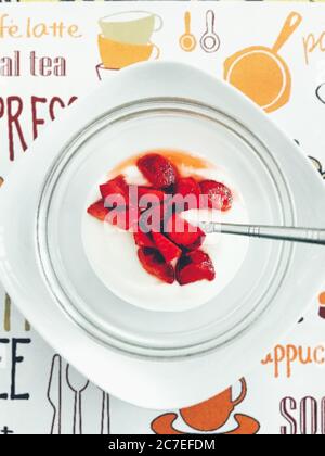 Colpo verticale ad alto angolo di gustoso yogurt con fragole tritate sopra accanto ad un cucchiaio d'argento Foto Stock