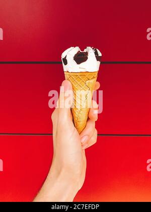 Una persona che tiene un cono di gelato al cioccolato e alla vaniglia con sfondo rosso Foto Stock