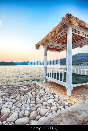 Tettoie e tende dal tetto di paglia sulla spiaggia Copacabana al tramonto a Dubrovnik. Ubicazione: Dubrovnik, Dalmazia, Croazia, Europa Foto Stock