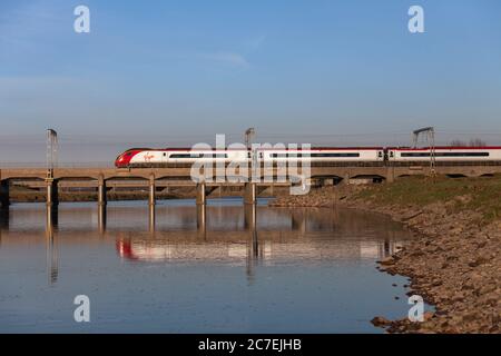 Una vergine treni pendolino di treno sulla linea principale della costa occidentale a Mossband a nord di Carlisle riflessa nelle acque del fiume Esk Foto Stock