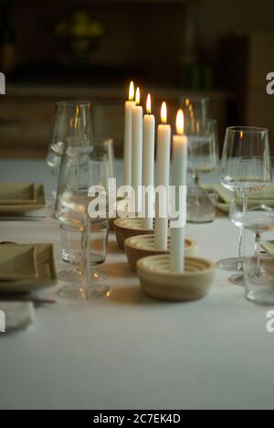 Scatto verticale di cinque candele bianche illuminate su un tavolo con bicchieri da vino e posate Foto Stock