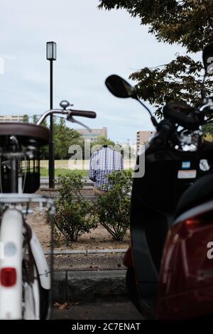 MATSUYAMA, GIAPPONE - 24 settembre 2019: Un colpo verticale di un solo maschio seduto sulla panchina nel parco con due moto Foto Stock