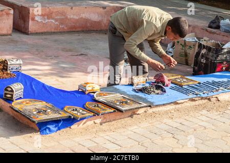 Un giovane falco mette in vendita i suoi beni - pendenti, scrigni e placche che rappresentano le porte - fuori dalla Moschea di Kutubiyya, nel centro di Marrakech. Foto Stock