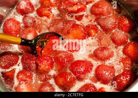 Сooking marmellata di fragole. Cucchiaio di legno in una ciotola di marmellata. Fragole mature in marmellata. Foto Stock