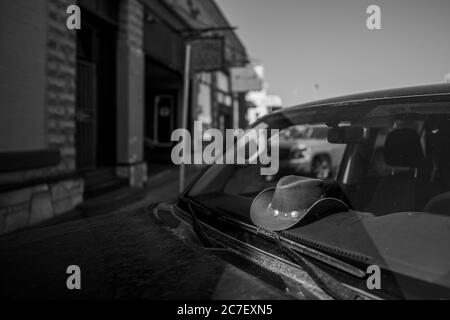 Colpo orizzontale in scala di grigi di un cappello da cowboy in auto Parcheggiato all'ombra su Route 66 Street Foto Stock