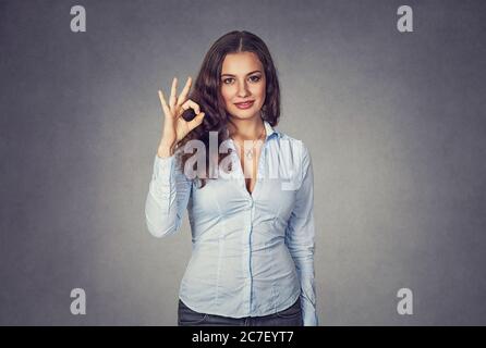 Donna felice che mostra ok segno gesto con mano isolata su sfondo grigio studio. Ritratto di primo piano. Emozione umana positiva, espressione del volto, lang del corpo Foto Stock