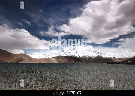 Scatto orizzontale del lago Karakol circondato da alte montagne coperte Nella neve in Cina Foto Stock