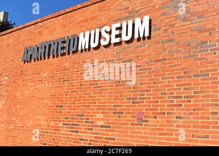 Un muro di mattoni rossi con un cartello per il Museo dell'Apartheid a Johannesburg, Sudafrica. Foto Stock