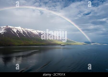 L'arcobaleno sul mare vicino alle montagne innevate e. una nave isolata Foto Stock