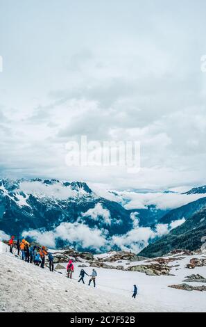 Gruppo di escursionisti che si preparano a continuare la loro escursione sotto il cielo bianco limpido in montagne innevate Foto Stock